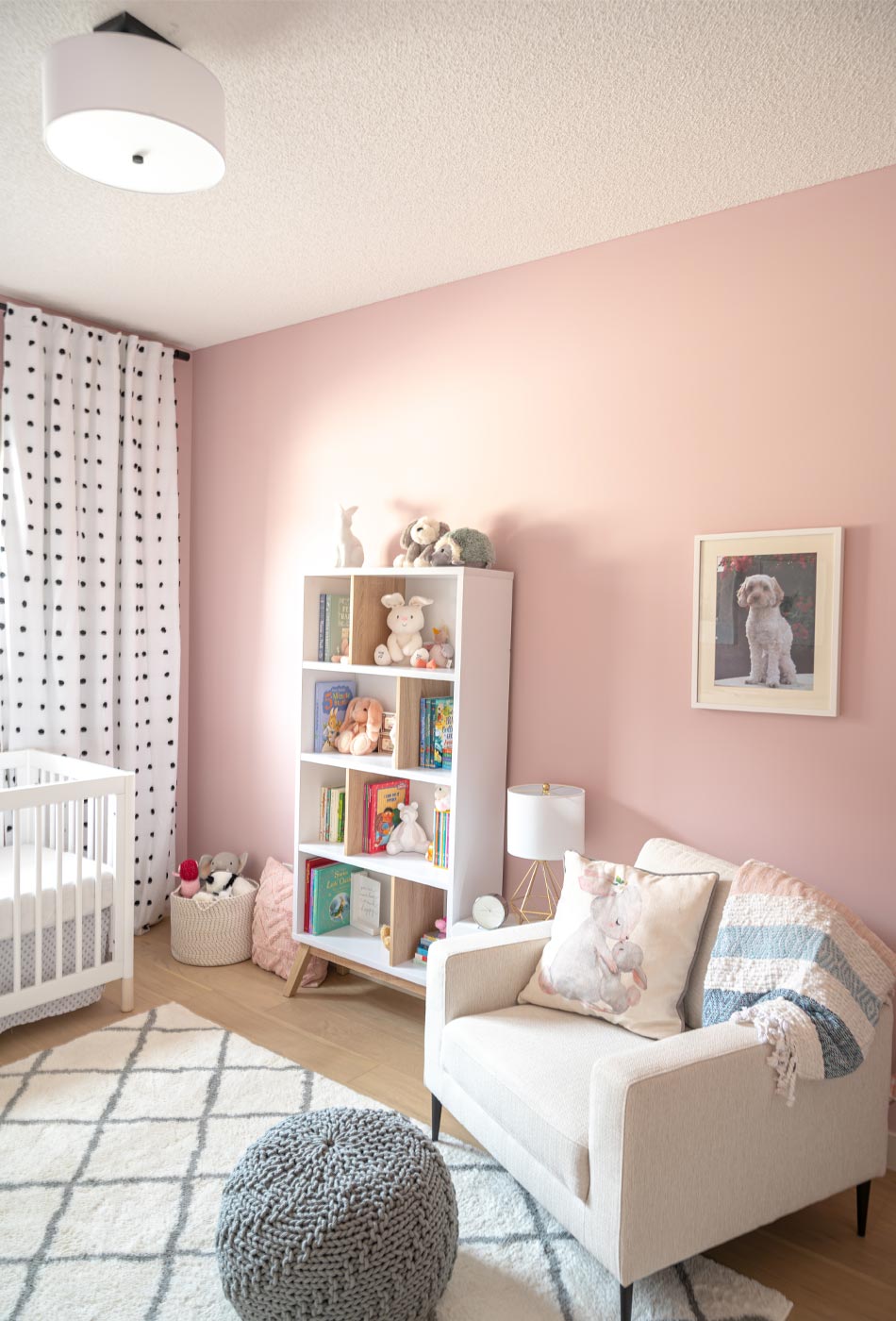 pink nursery, feminine nursery, baby girl room, baby girl nursery, white crib, white crib pink walls, pink walls nursery, modern feminine nursery, modern girls room, modern baby girl room, pompom curtains nursery, white chair nursery, nursery bookshelf, nursery modern bookshelf